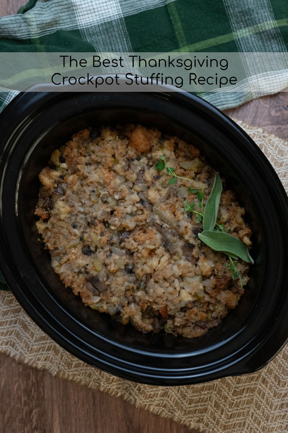 fully cooked thanksgiving stuffing in a black crockpot on a wood table with a green plaid kitchen towel in the top of the photo