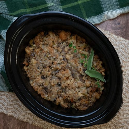 crockpot stuffing in a black crockpot dish on a wood table with a green plaid kitchen towel in the top half of the photo