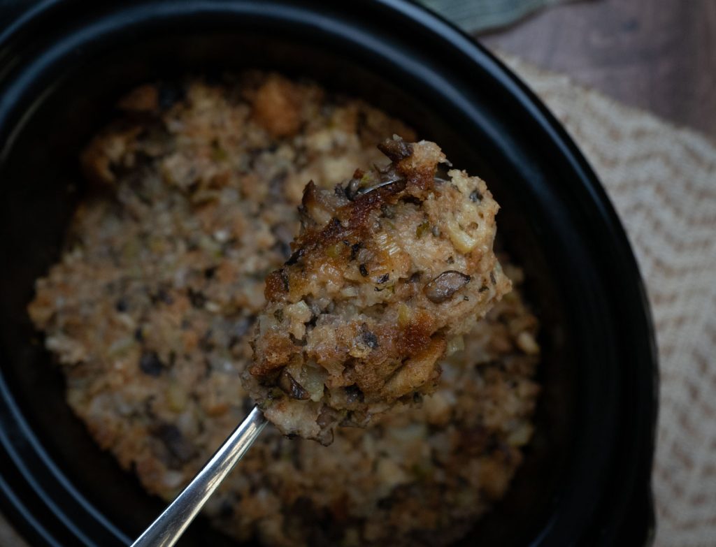 spoonful of stuffing held up over a full crockpot of stuffing 