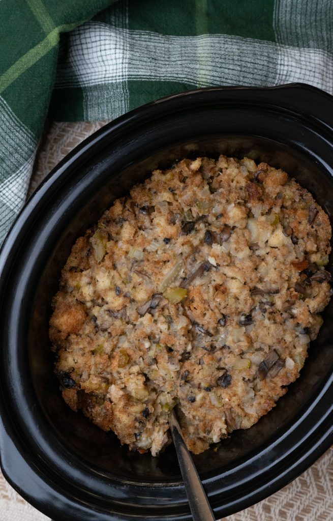 crockpot with stuffing in it fully cooked, a green plaid kitchen towel is in the top half of the photo