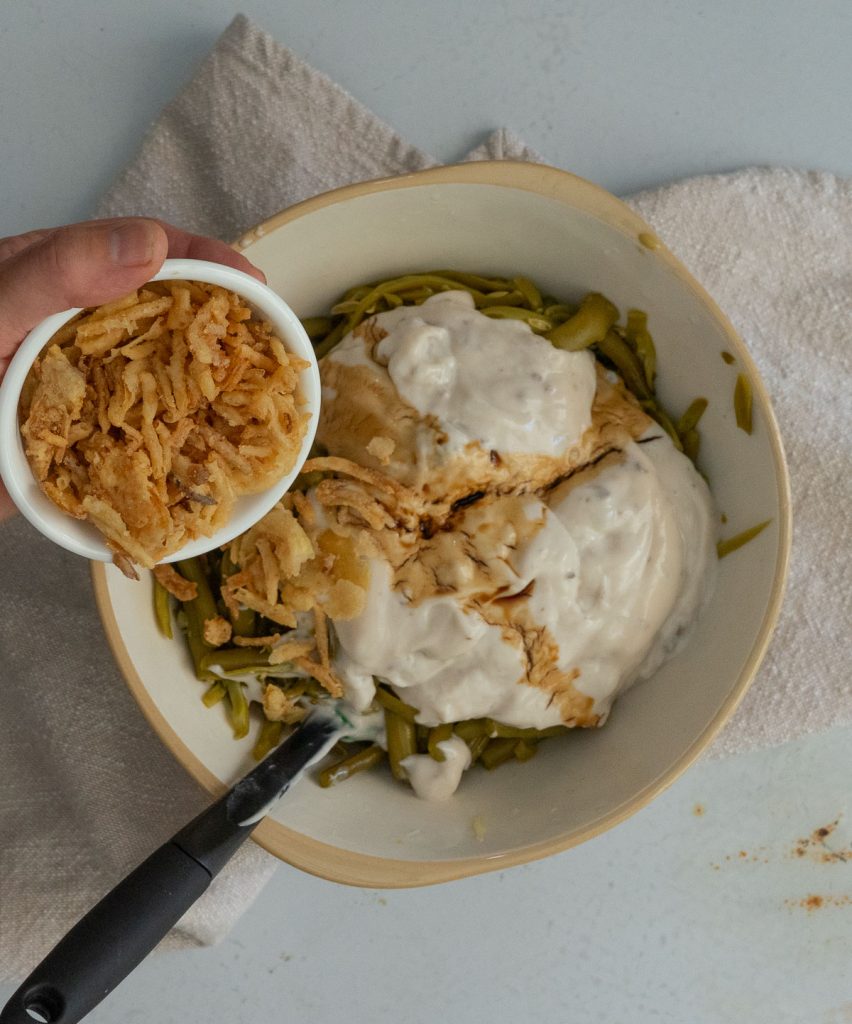 adding 1 cup of french fried onions to the bowl with green beans and soup