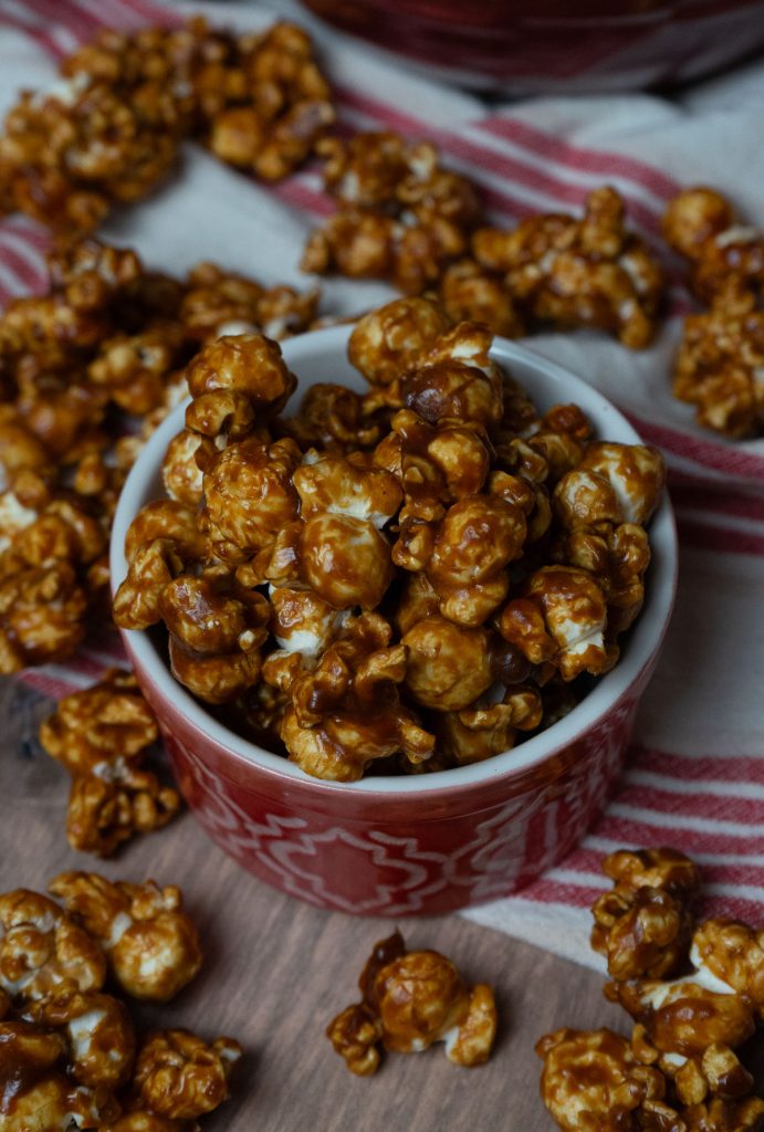 gingerbread caramel corn in a red dish with caramel corn strewn around the table a red and white striped cloth is laying in background