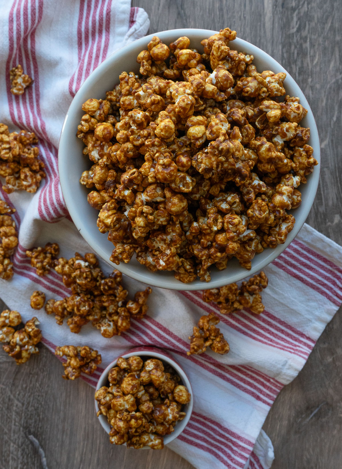 large bowl full of gingerbread caramel corn on a red and white striped cloth, with a small dish of caramel corn on the lower left hand side