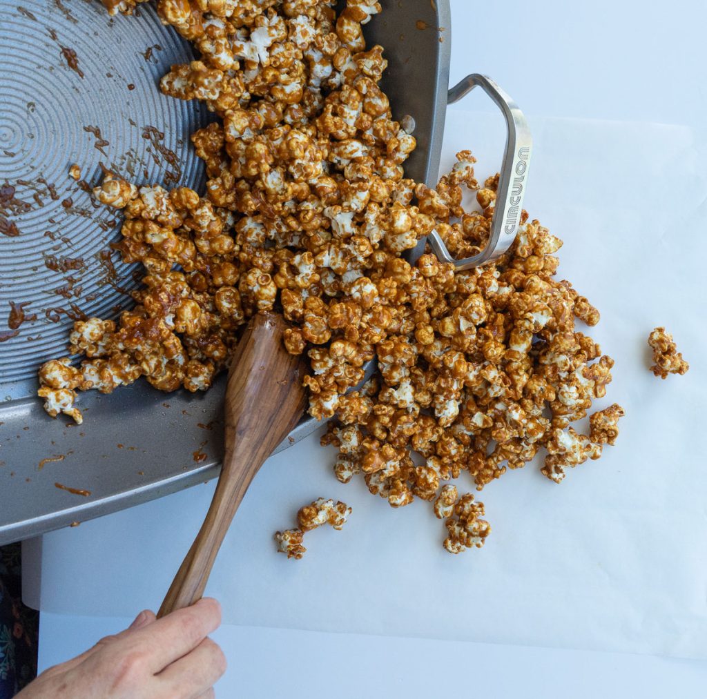 pouring baked gingerbread caramel corn out onto parchment paper