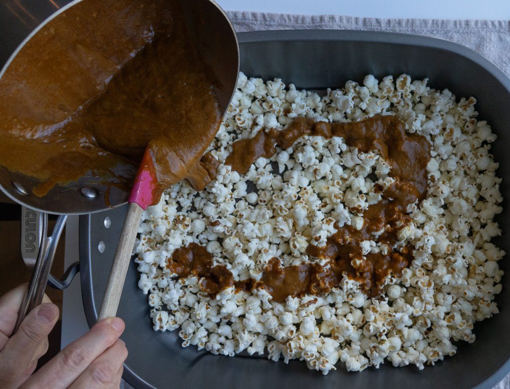 pouring caramel sauce over popcorn in roasting pan