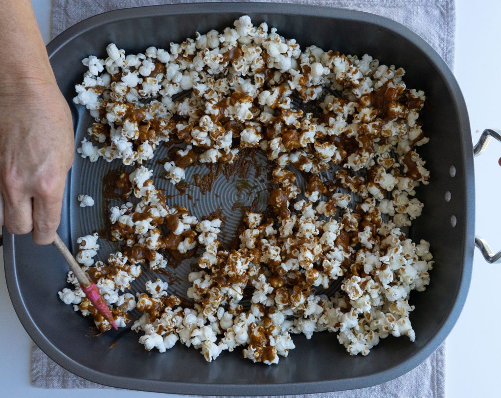 Stirring caramel sauce and popcorn together in a large roasting pan with a spatula