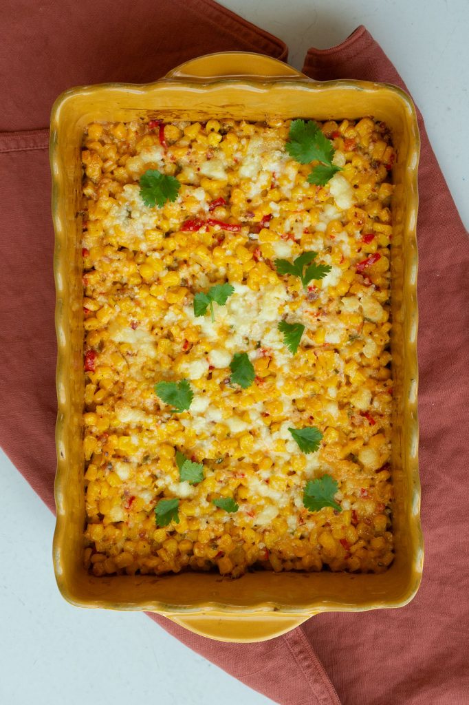 Easy Mexican Street Corn Casserole in a yellow baking dish on a rust colored napkin on a gray countertop