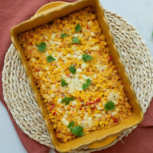 Mexican corn bake in a yellow rectangle dish on a round rattan trivet with a rust colored rush on a gray counter top