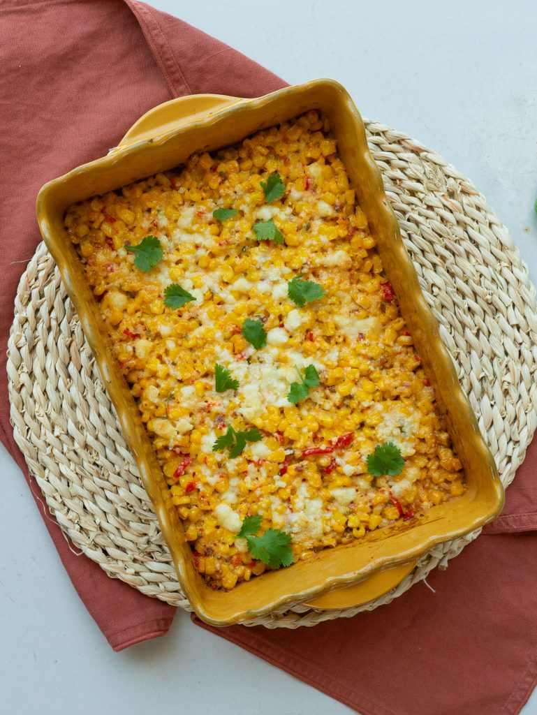Mexican corn bake in a yellow rectangle dish on a round rattan trivet with a rust colored rush on a gray counter top