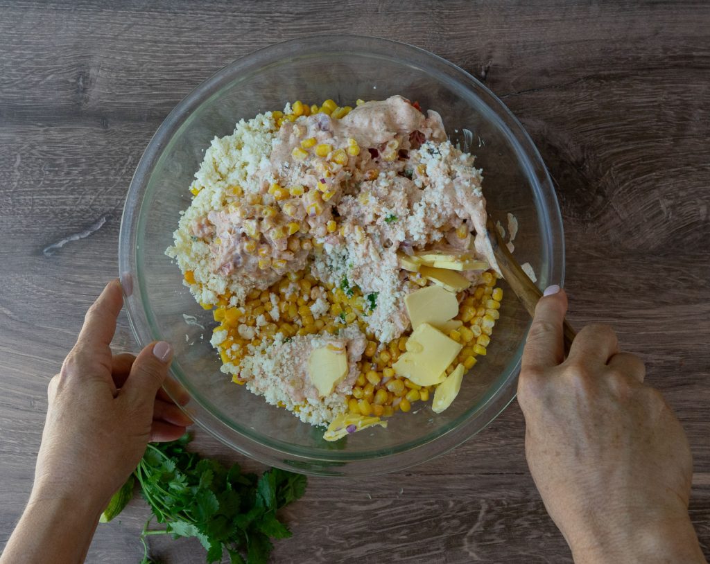 stirring all the ingredients of the mexican corn casserole together in a glass bowl on a wood counter