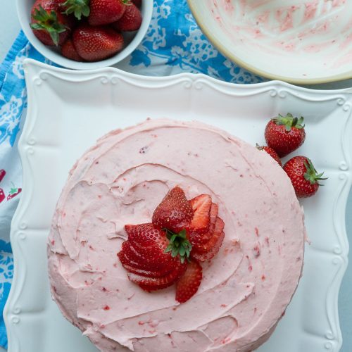 top view of strawberry cake with a bowl of whole fresh strawberries off the the upper left