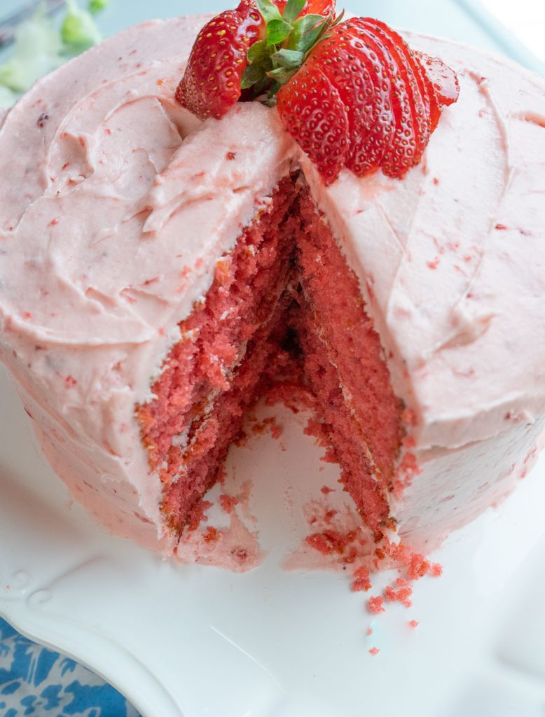 strawberry cake on a white platter with one piece cut out