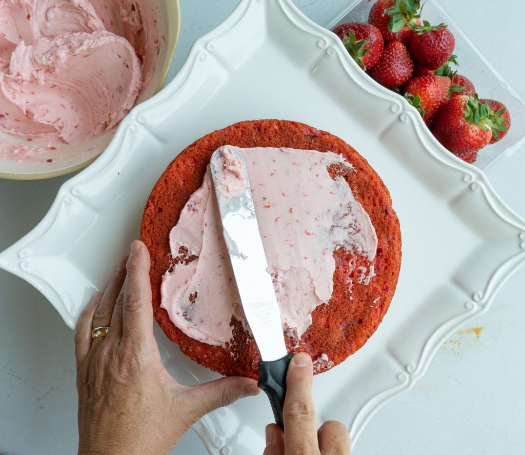 frosting strawberry cake with fresh strawberries and bowl of frosting in upper corners of the photo