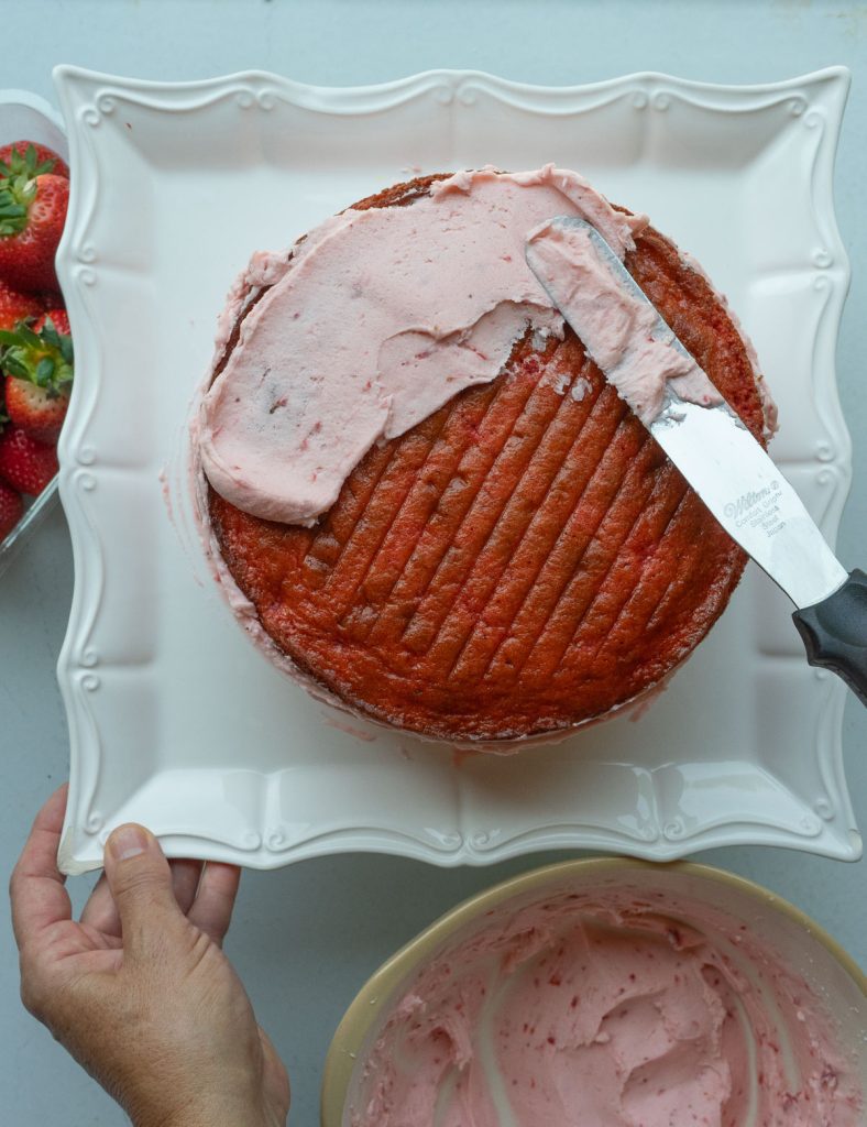 frosting the top of the strawberry cake on a white platter