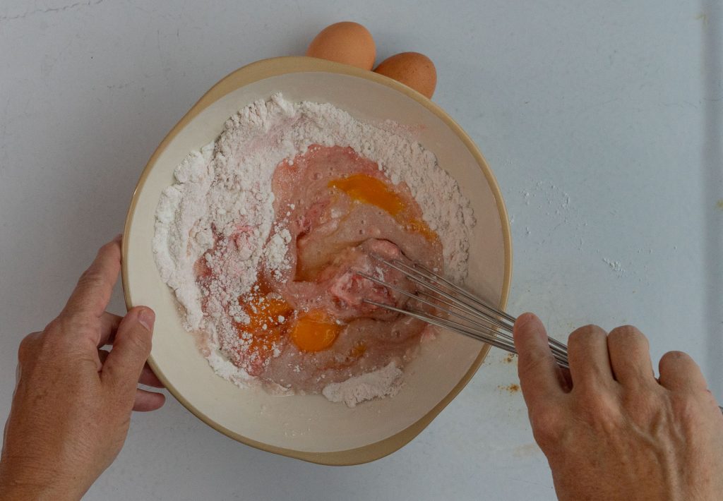 mixing in vegetable oil and eggs into dry ingredients hand off the the lower right is whisking ingredients