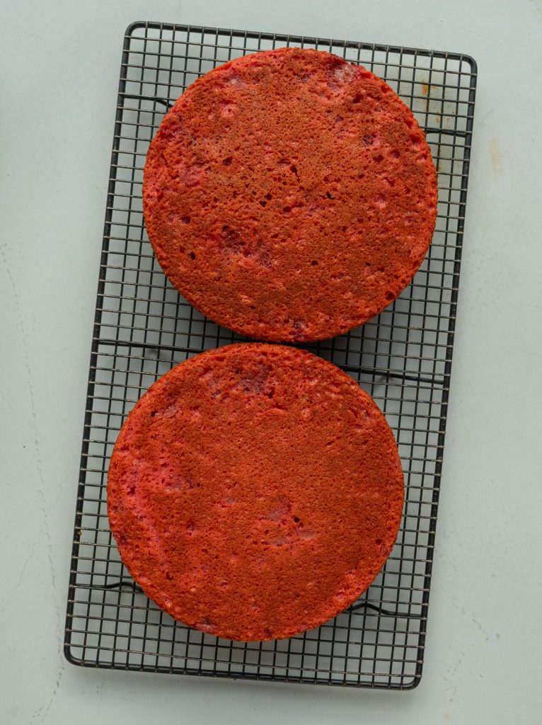 two round strawberry cakes cooling on a bakers rack