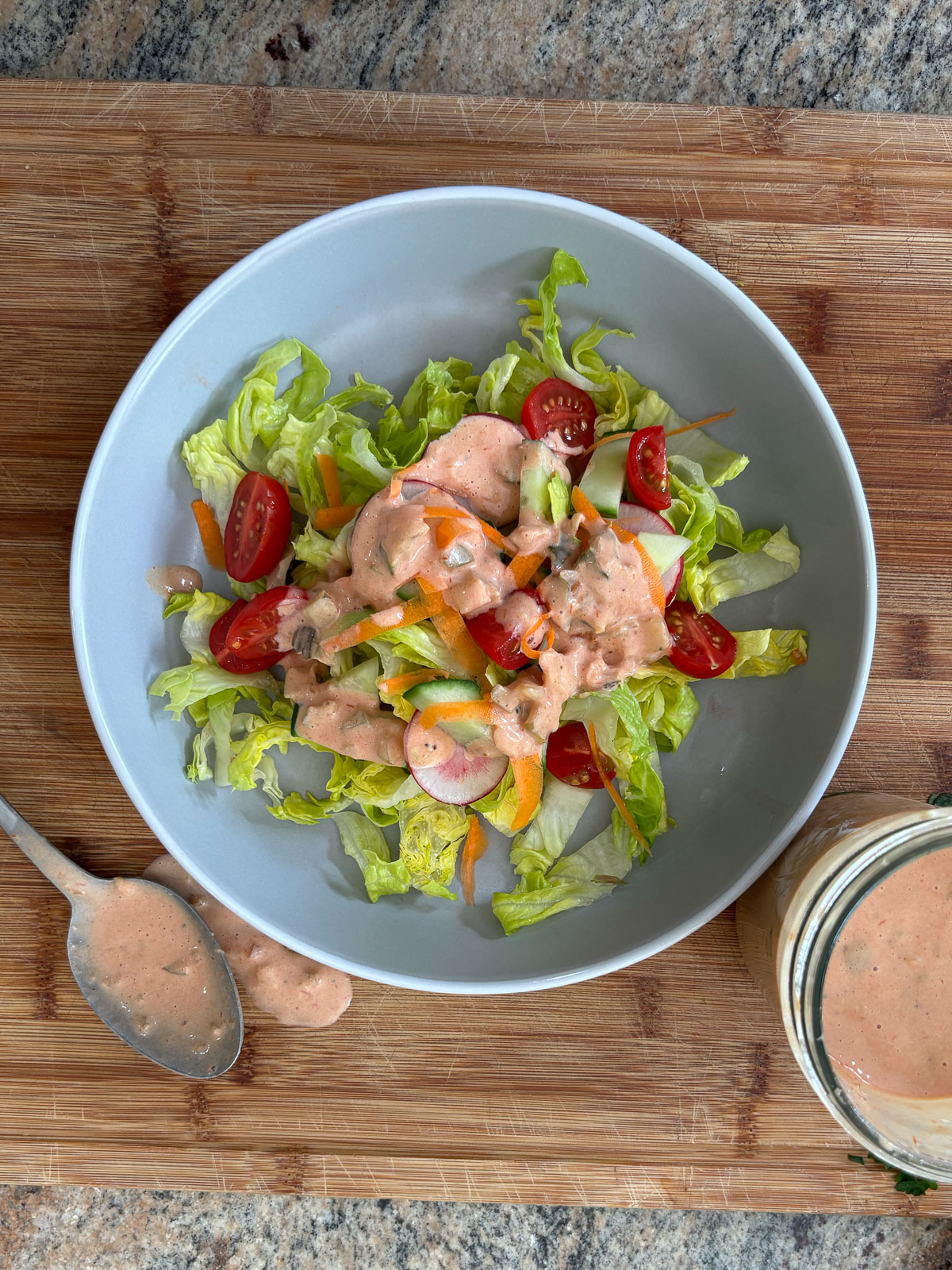 plate of salad with thousand island dressing on it, plate is on a wood cutting board with a bowl of dressing off to the side