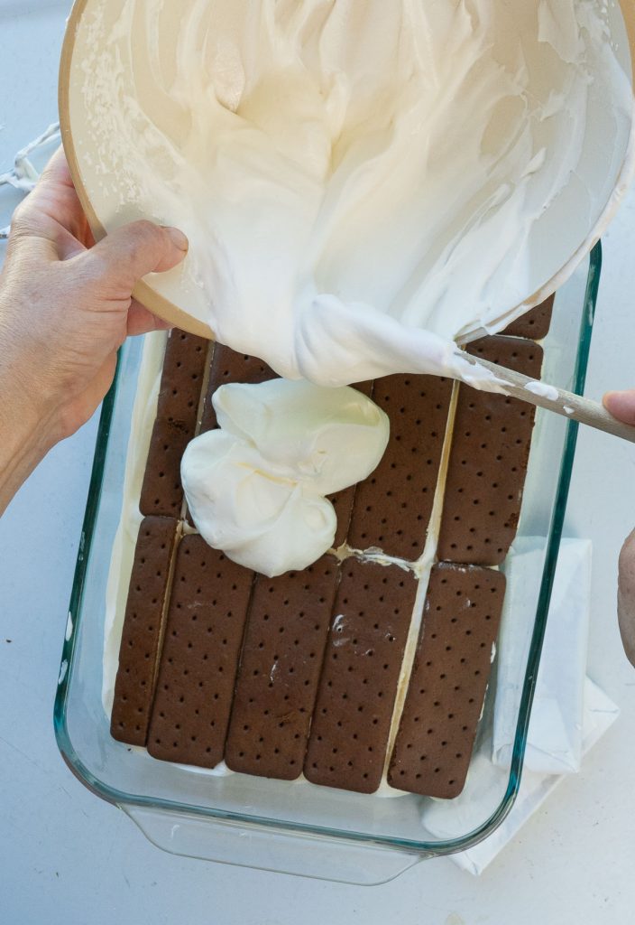 spreading whipped cream over the first layer of ice cream sandwiches in glass dish