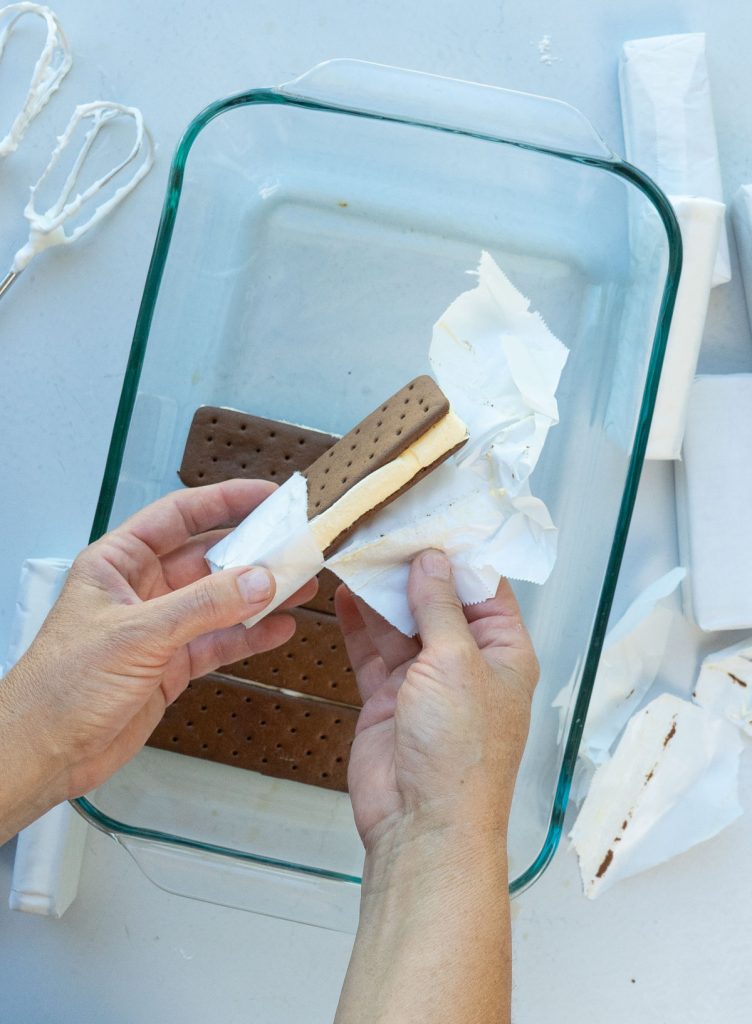 unwrapping ice cream sandwiches and layering them in the bottom of glass dish