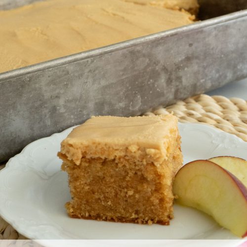 peanut butter snack cake on a white plate on a rattan place mat with 9x13 cake pan with one piece missing