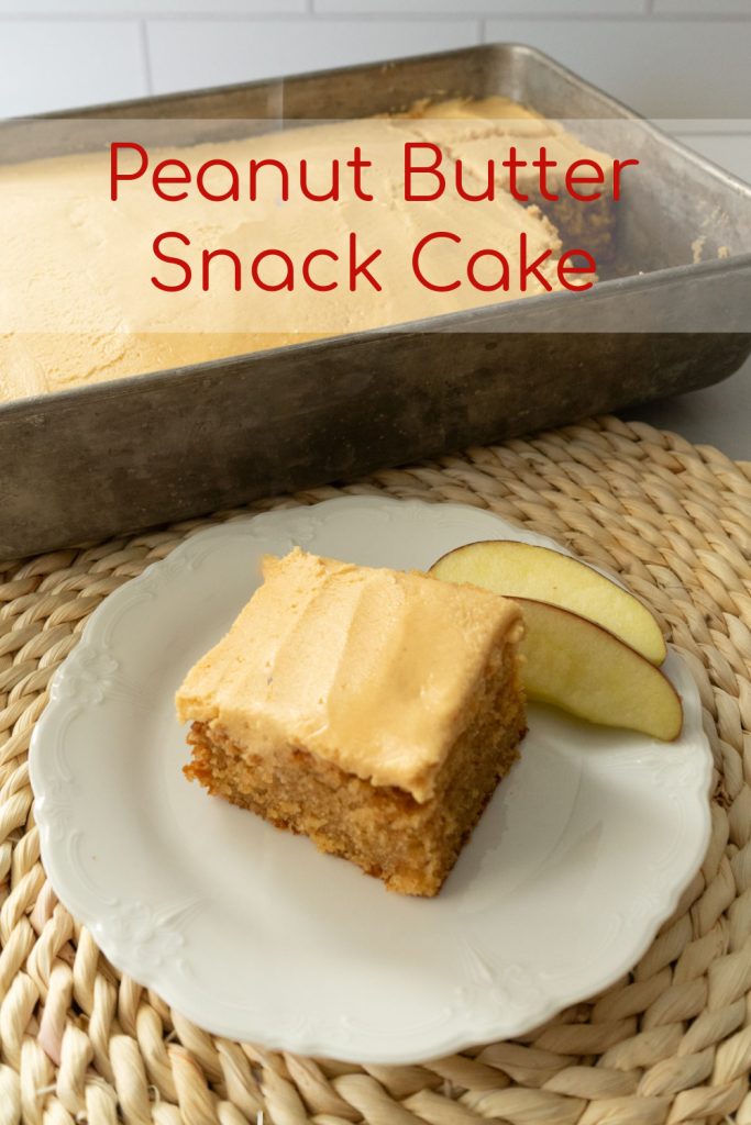 piece of peanut butter snack cake on a white plate on top of a rattan place mat with 9x13 cake pan in back ground with one piece take out of the corner