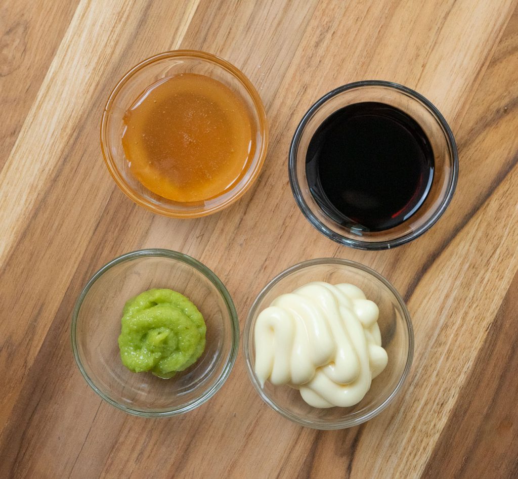 sauce ingredients, honey, soy sauce, wasabi, mayonnaise on a wood cutting board