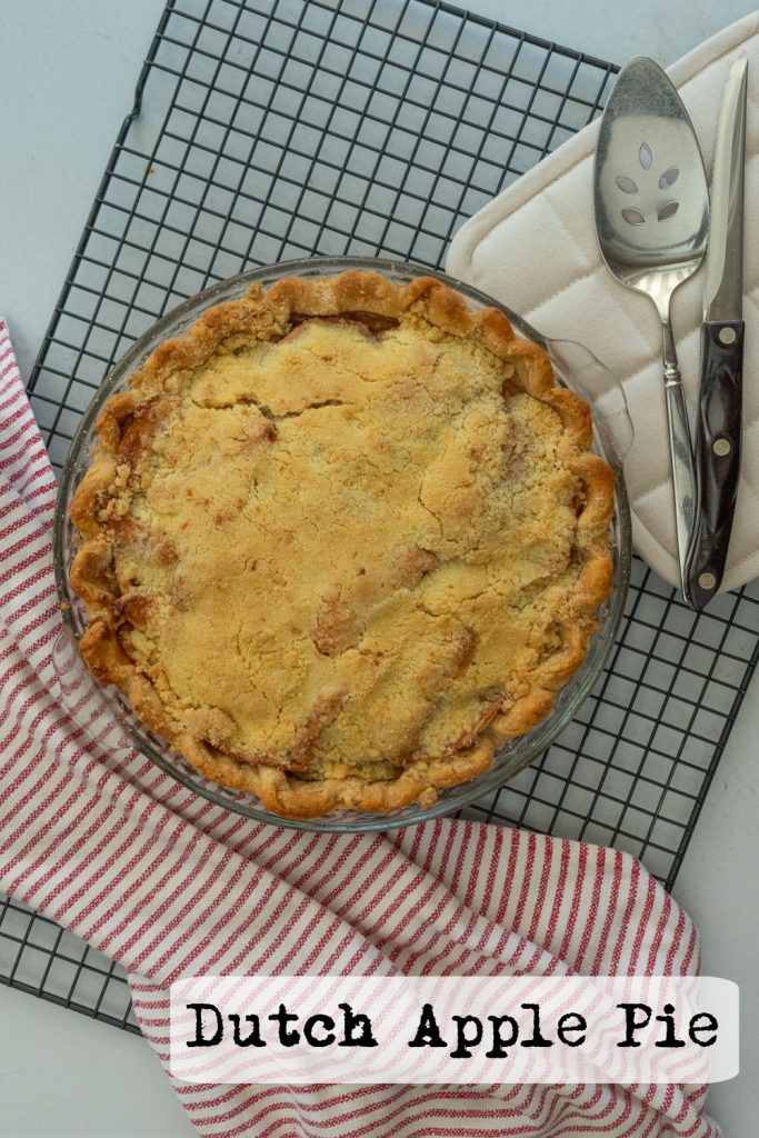 whole dutch apple pie uncut on a cooking rack with server and knife on the upper righthand side of the photo