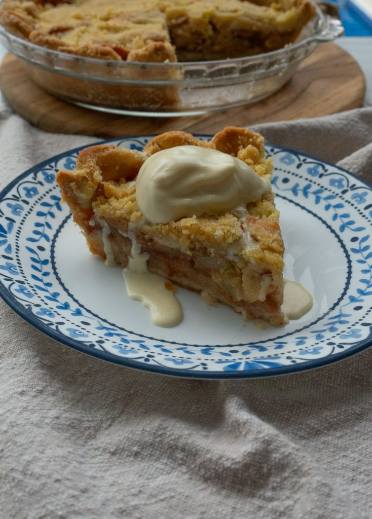 slice of dutch apple pie on a plate with ice cream dripping off the side whole pie in background