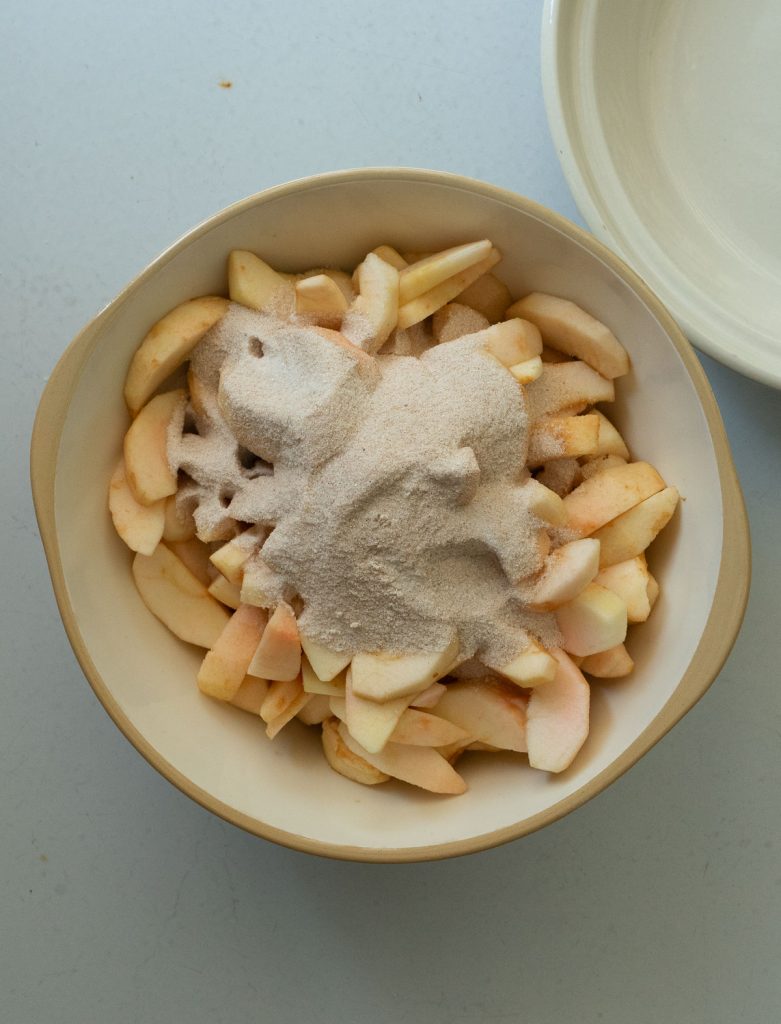 apple slices in a bowl with spices, sugar and flour on top before mixing