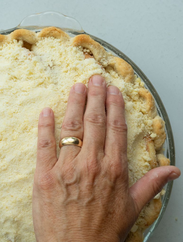 hand pressing crumble topping down into apples