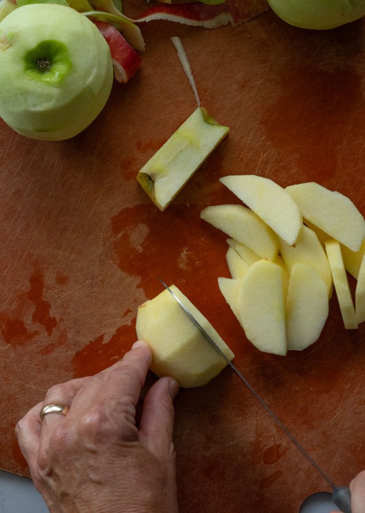 slicing apples on a brown cutting board for dutch apple pie 