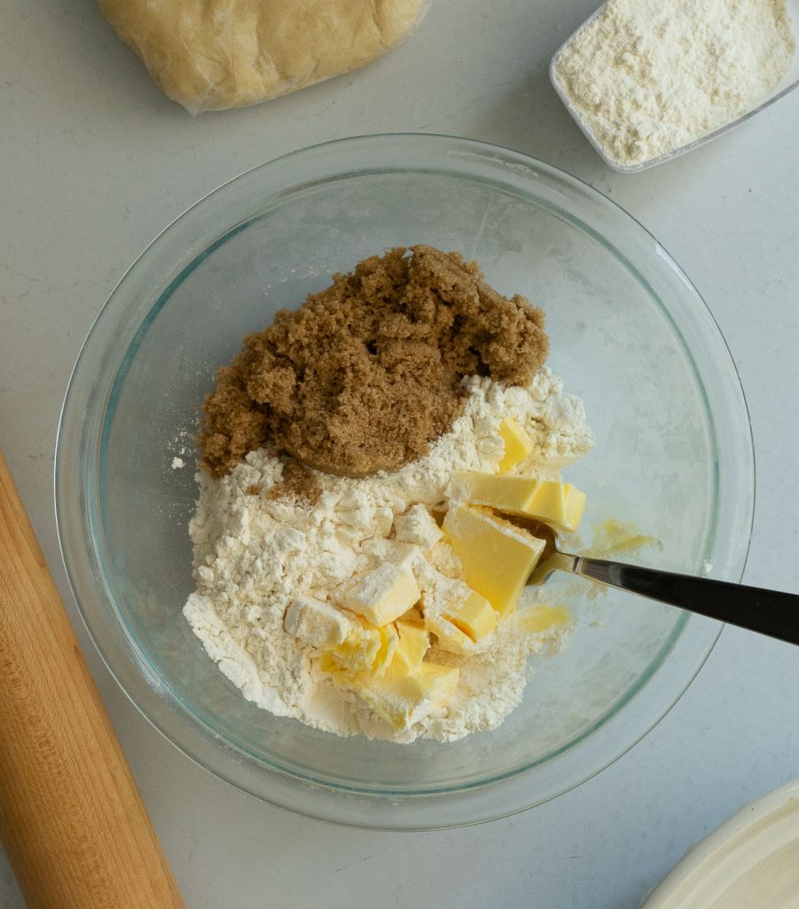 making crumble topping in a glass bowl brown sugar, flour, and butter are being mixed togeter