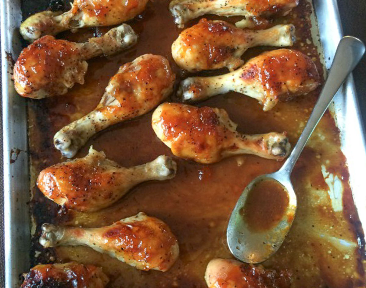 chicken legs on a sheet pan baked in bbq sauce , spoon with sauce on it off the right side of the pan