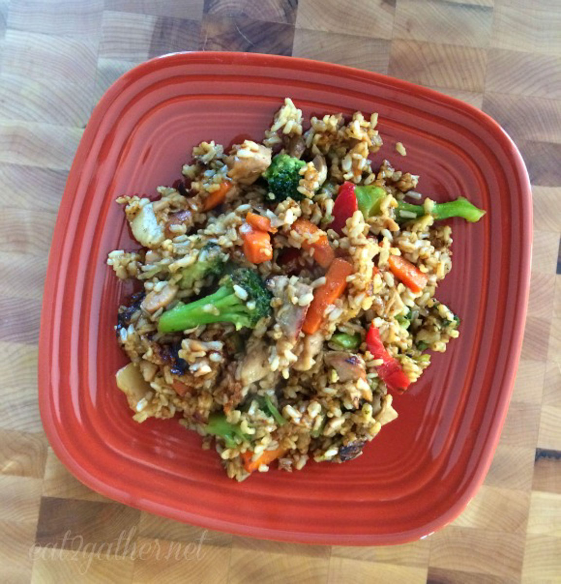 chicken stir-fried rice on a rust colored plate on a butcher block