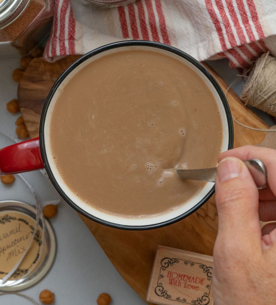 hand on the right side of a cupping stirring caramel cappuccino 