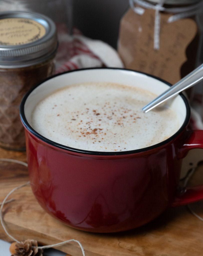 red mug on a piece of wood, with mason jars full of caramel cappuccino mix in the background.