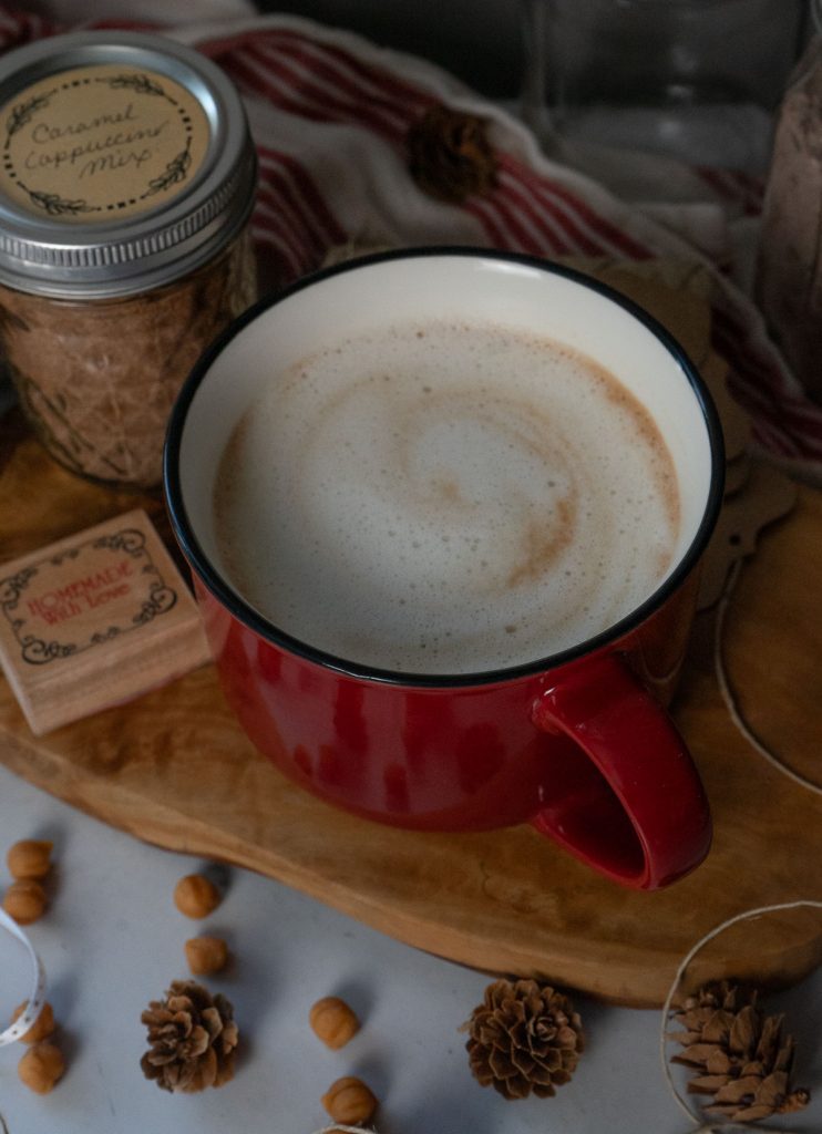 red mug on a wooden board full of caramel cappuccino decorations of pinecones and ribbon around the cup