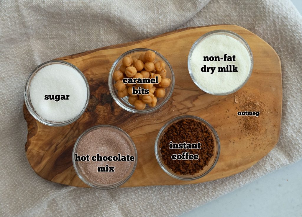 ingredients for caramel cappuccino mix on a wood cutting board with a tan cloth background