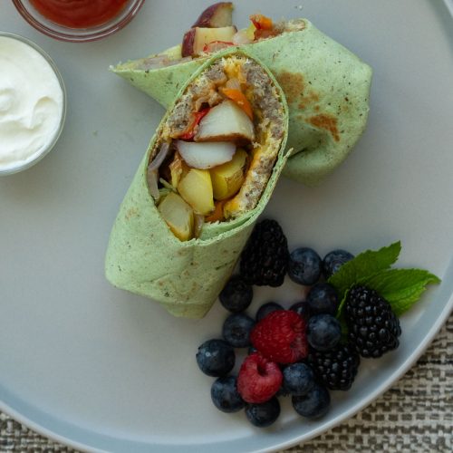 Breakfast burrito sliced in half with one half resting on the other half so you can see the egg and potatoes on the inside, next to it is berries with mint leaves