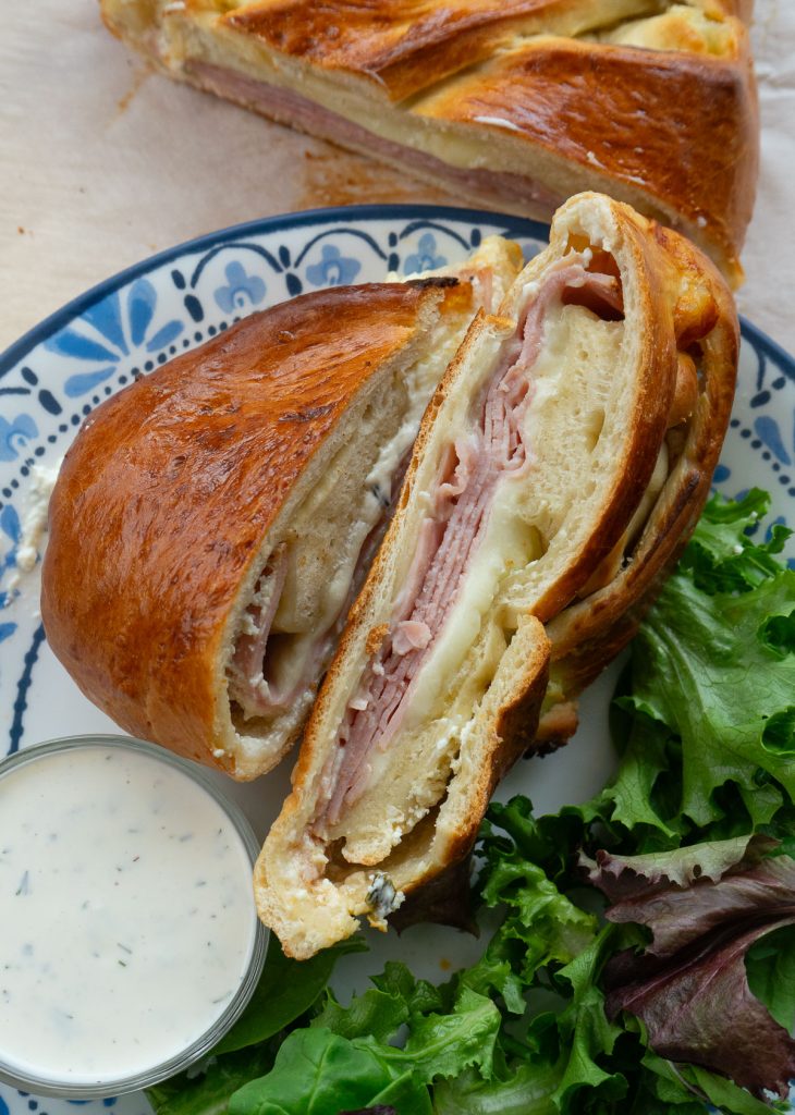 slices of baked ham sandwich on a plate with salad and a side of ranch dressing