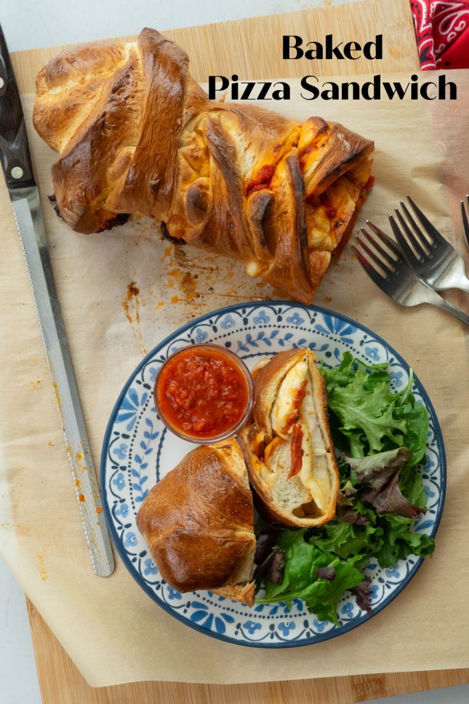 Baked Pepperoni Pizza sandwich on a cutting board with a plate with two slices of sandwich, dish of pizza sauce, and a green salad