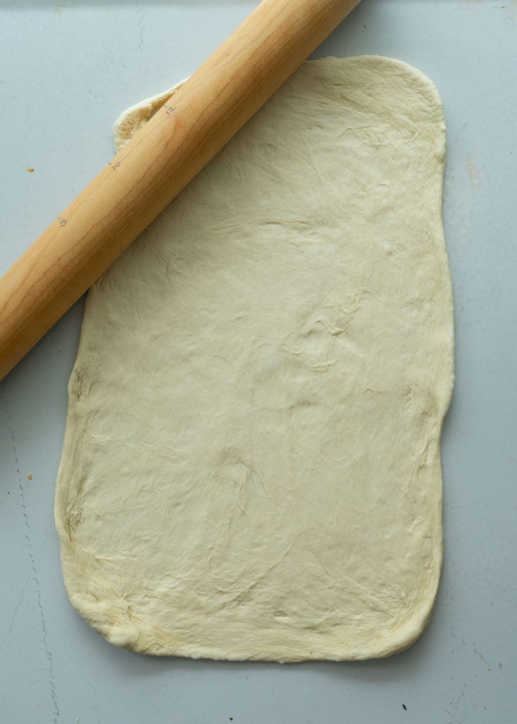 roll bread dough out on countertop with rolling pin in the upper left corner of photo