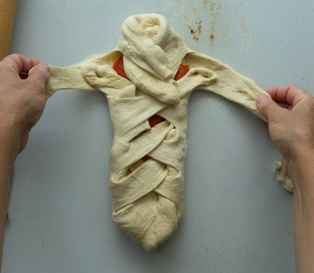 assembling pizza sandwich, braiding bread dough over pizza ingredients 