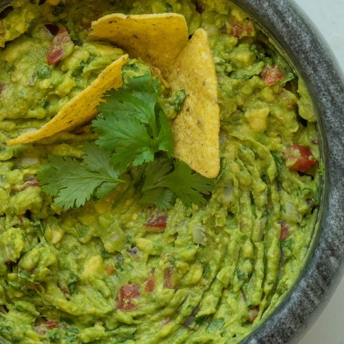 bowl of guacamole garnished with cilantro and tortilla chips