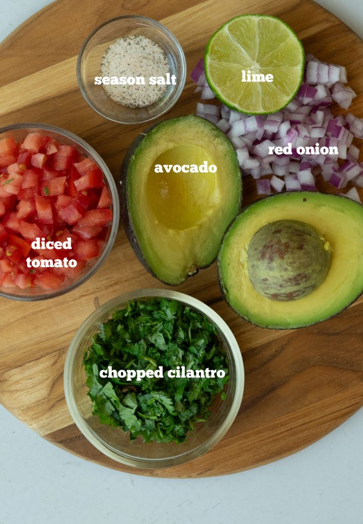 ingredients for guacamole on a round wood cutting board that is on a gray countertop