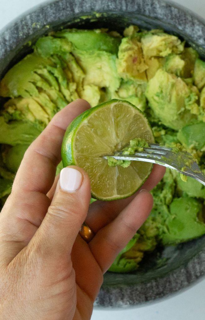 lime in left hand with right hand sticking a fork into the lime and twisting to release all the juices into the smashed avocados