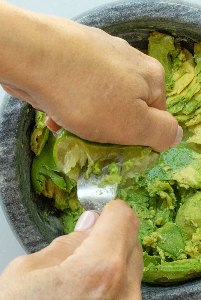 squeezing lime juice over smashed avocados in a bowl