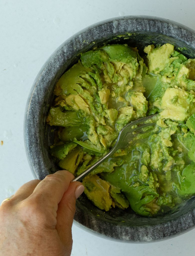 mixing lime juice into smashed avocados that are in a dark gray stone bowl on a gray countertop