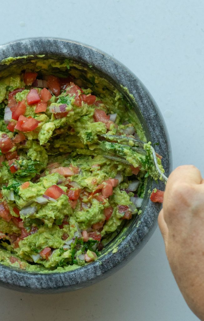 right hand stirring guacamole in dark gray stone bowl on a gray countertop