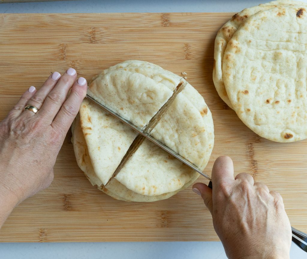 pita bread on a wood cutting board. Pita bread being cut with a knife